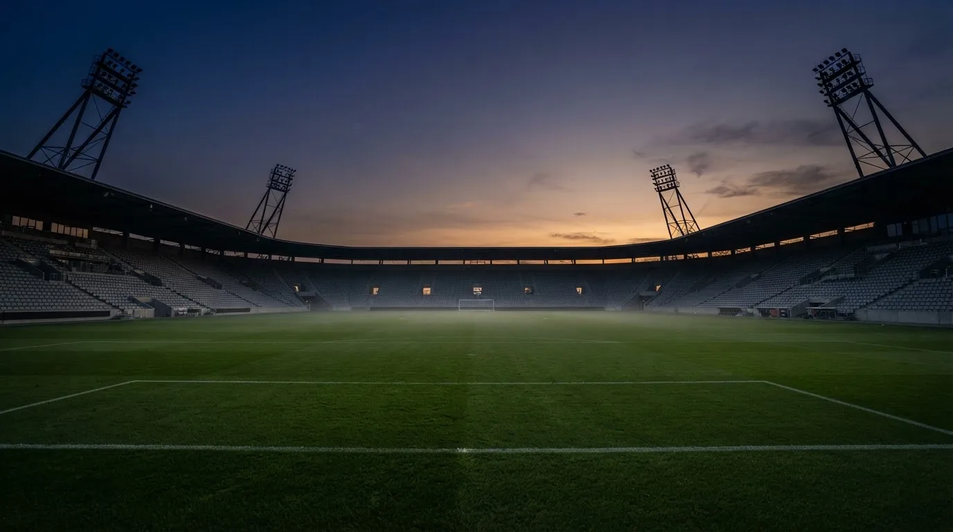 An empty football stadium with floodlight masts at dusk