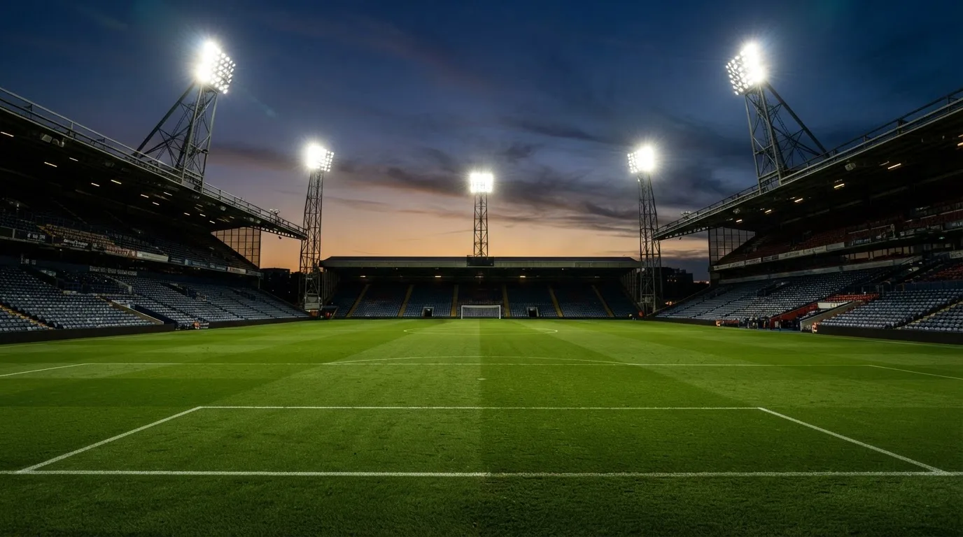 An empty football stadium with floodlight masts at dusk