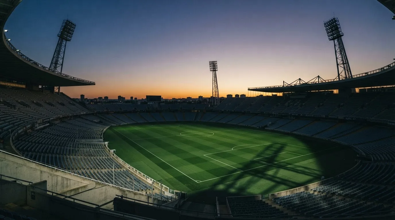 An empty football stadium with floodlight masts at dusk