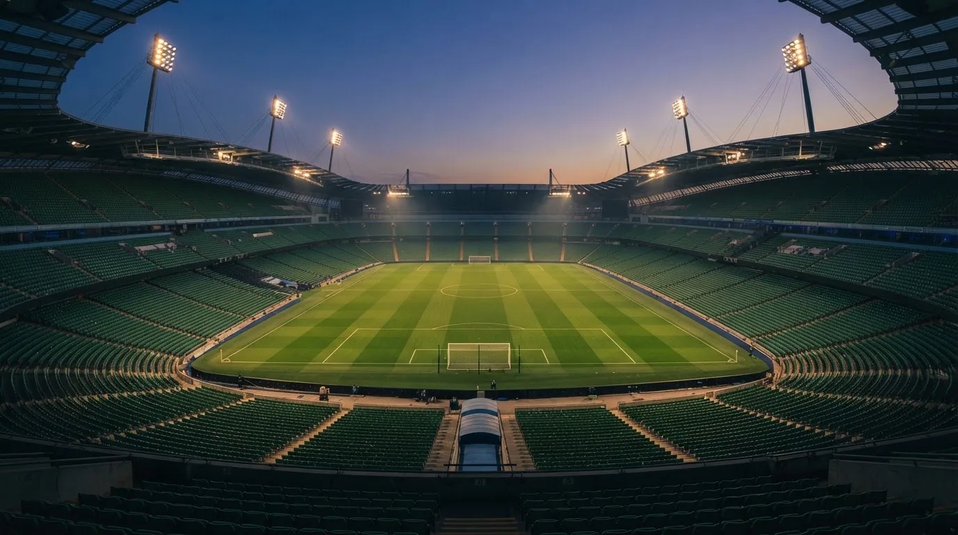 An empty football stadium with floodlight masts at dusk