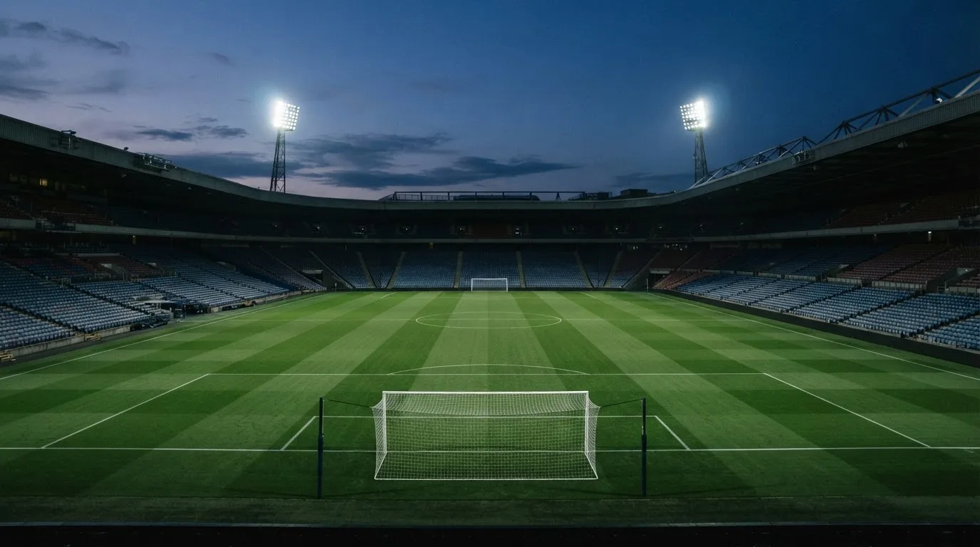 An empty football stadium with floodlight masts at dusk