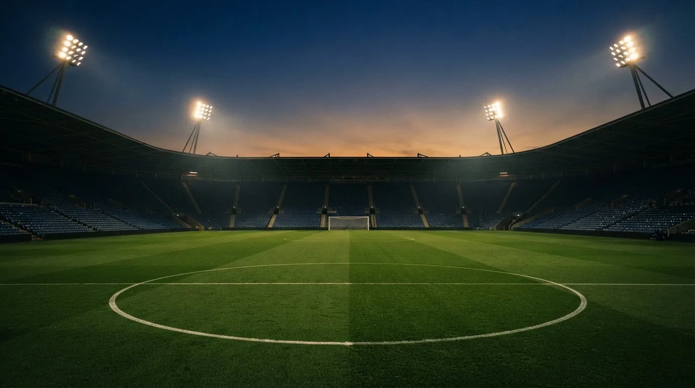 An empty football stadium with floodlight masts at dusk